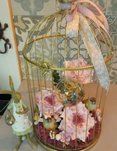 Jaula dorada decorativa con lazos rosas y flores de tela en su interior